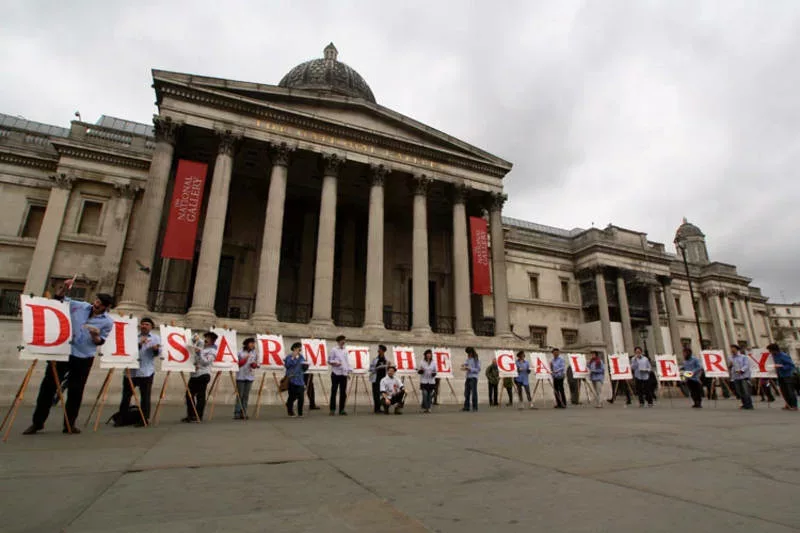 activists dress as steryotypical artists in berets to spell a message on easels outside the national gallery, It says disarm the gallery.