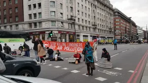 People sit across a road stopping traffic as part of a protest against air pollution.