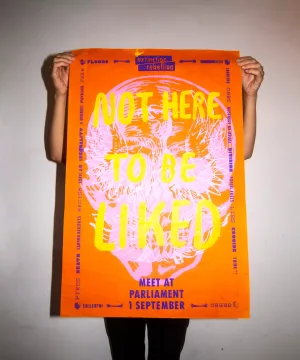 Person holding up a bold protest poster with the phrase "not here to be liked" as part of an environmental action campaign.
