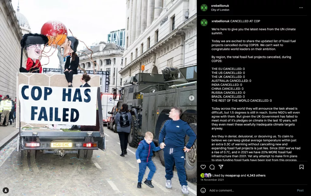 Protesters display a banner saying "cop has failed" on the back of a trailer, surrounded by activists and a large puppet, during a climate change demonstration in an urban setting.